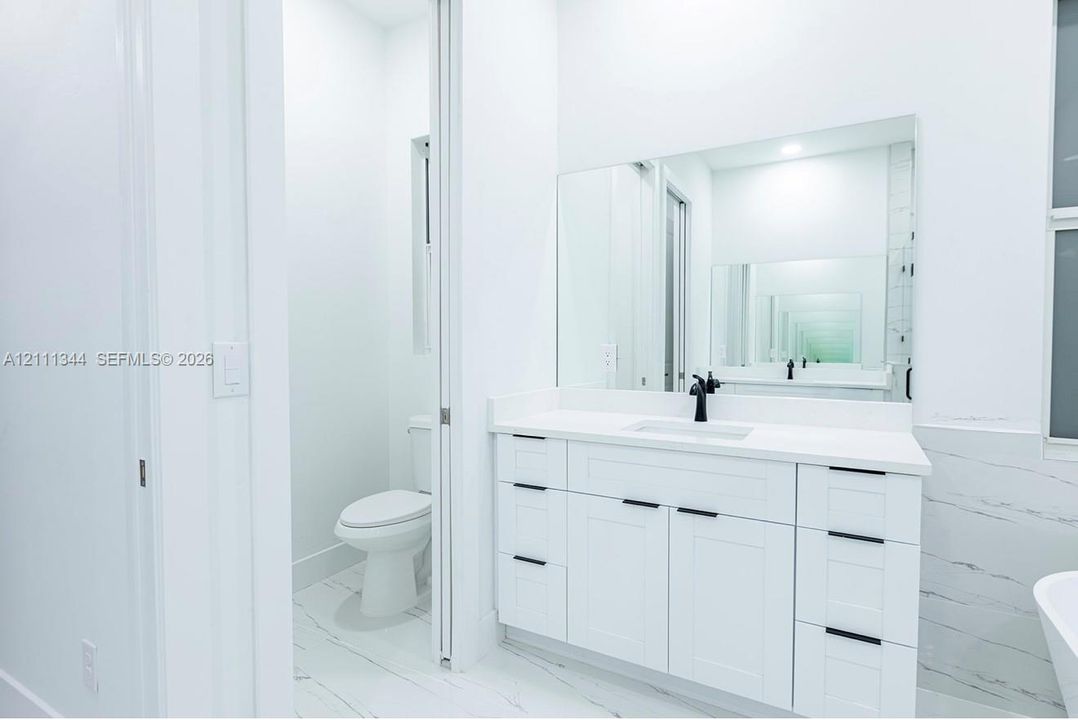 White vanity with shaker-style cabinetry, quartz countertop, matte black hardware, integrated sink, and large wall-mounted mirror