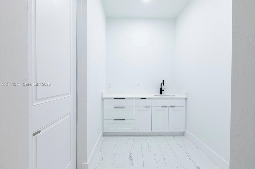 Utility space featuring white shaker-style cabinetry, solid-surface countertops, an undermount sink with a matte black faucet, and large-format tile flooring