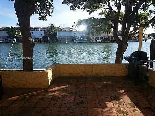 Waterfront patio featuring terra cotta tile flooring, a low-profile masonry retaining wall, and mature shade trees