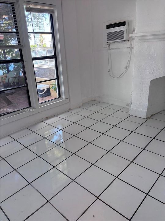 Glossy white ceramic tile flooring, multi-pane window with dark frames, wall-mounted air conditioning unit, and textured white wall finish