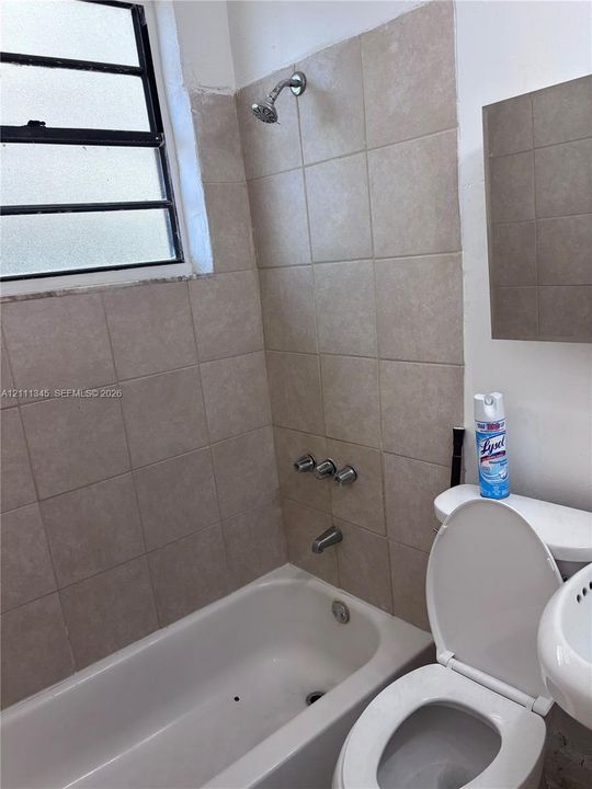 Bathroom featuring ceramic tile shower surround, integrated tub, metal plumbing fixtures, and a framed window