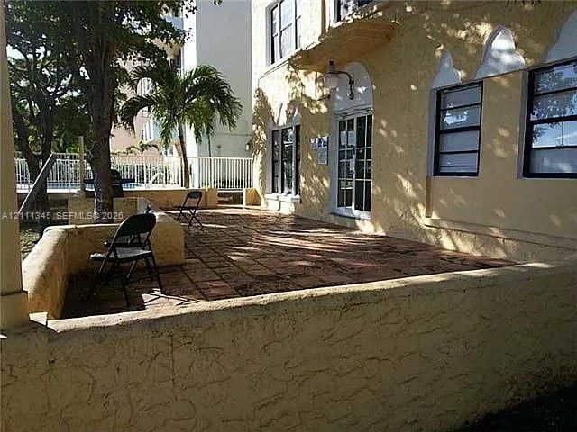 Stucco exterior featuring a spacious tiled patio, arched window detailing, and a low-profile masonry perimeter wall