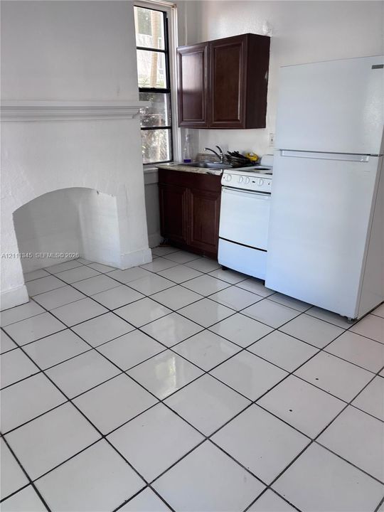 Kitchen featuring white ceramic tile flooring, dark wood-finish cabinetry, a built-in white stove, and a decorative fireplace mantel