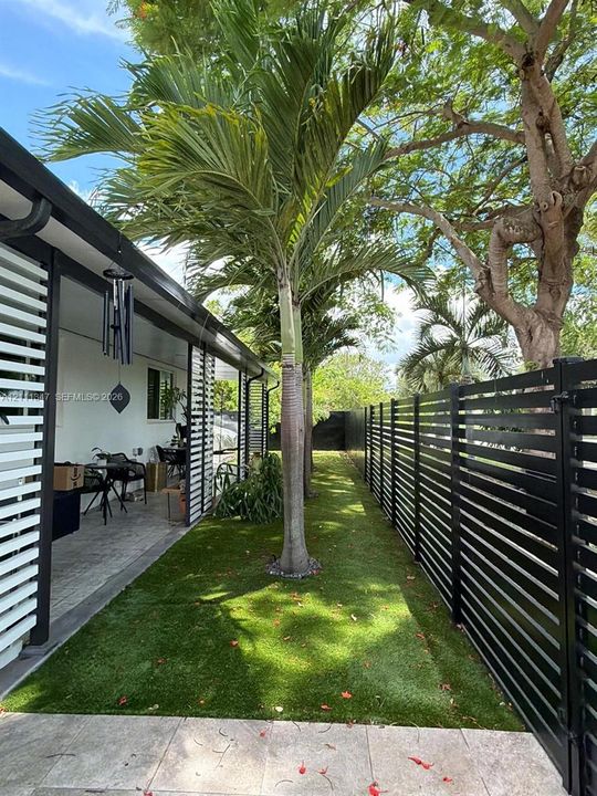 Outdoor space featuring a covered patio, artificial turf, mature palm trees, and horizontal slat privacy fencing