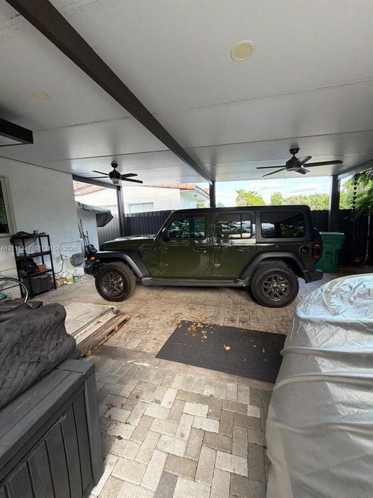 Covered patio area featuring a paver stone floor, dual ceiling fans, and dark-finished structural beams