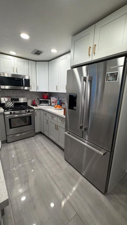 Kitchen featuring white shaker-style cabinetry, stainless steel appliances, polished stone-look tile flooring, and a stone mosaic backsplash