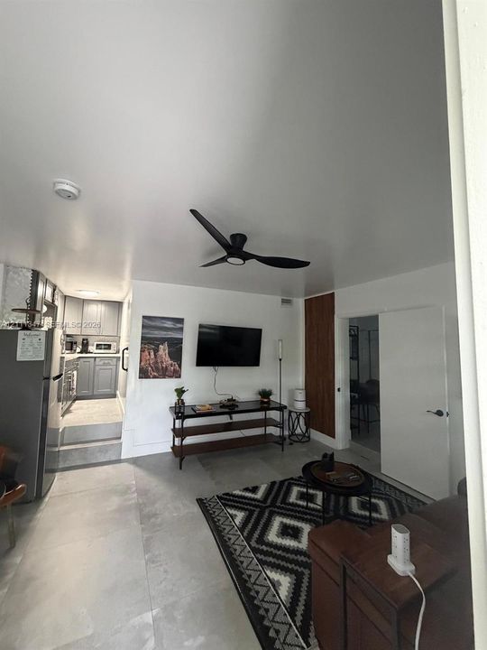 Living space featuring large-format tile flooring, a modern black ceiling fan, and a vertical wood-slat accent wall