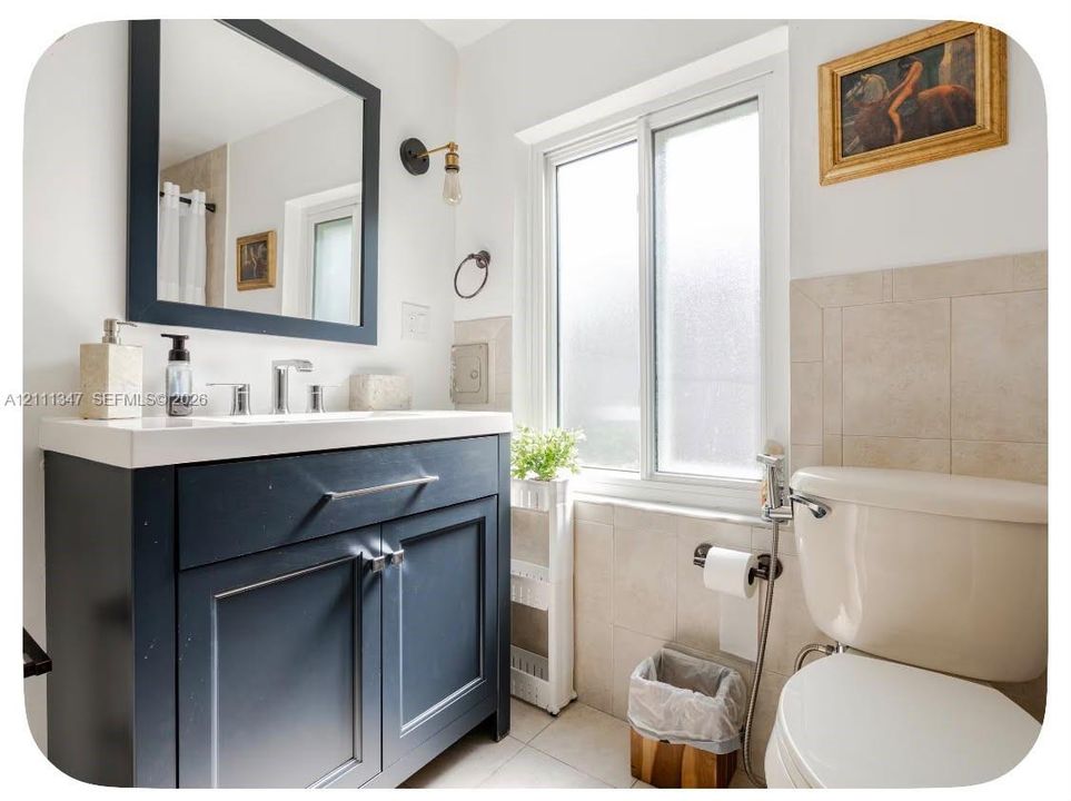 Navy blue vanity with a rectangular sink, wall-mounted matte black light fixture, framed mirror, and light-toned ceramic tile backsplash