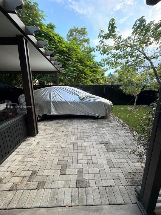 Covered carport featuring a structural beam frame and herringbone-patterned stone paver flooring