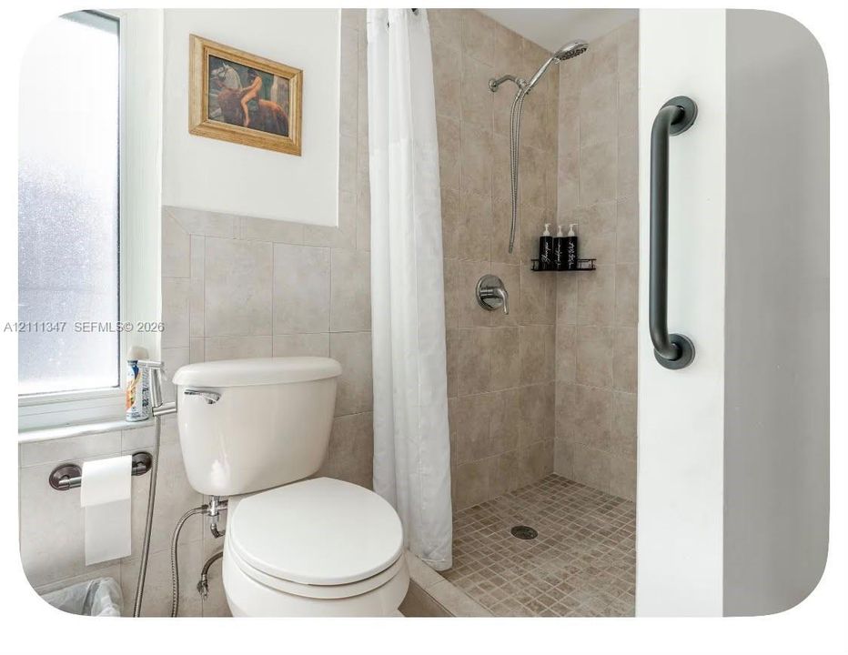 Bathroom featuring a walk-in shower with tile surround, mosaic tile flooring, a mounted grab bar, and a window