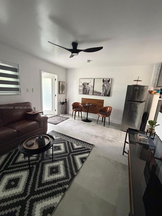 Living area featuring large-format tile flooring, matte black modern ceiling fan, and window with zebra-style shade