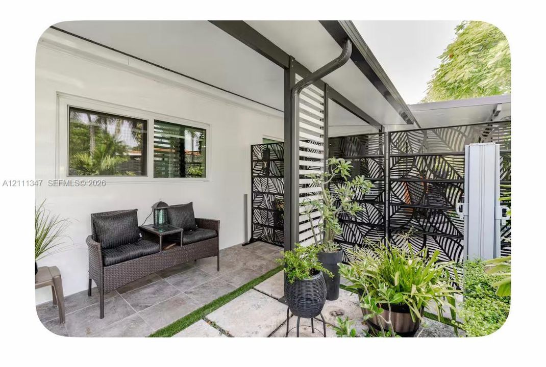 Covered patio featuring slate-style tile flooring, decorative metal privacy screens, and integrated horizontal slat siding