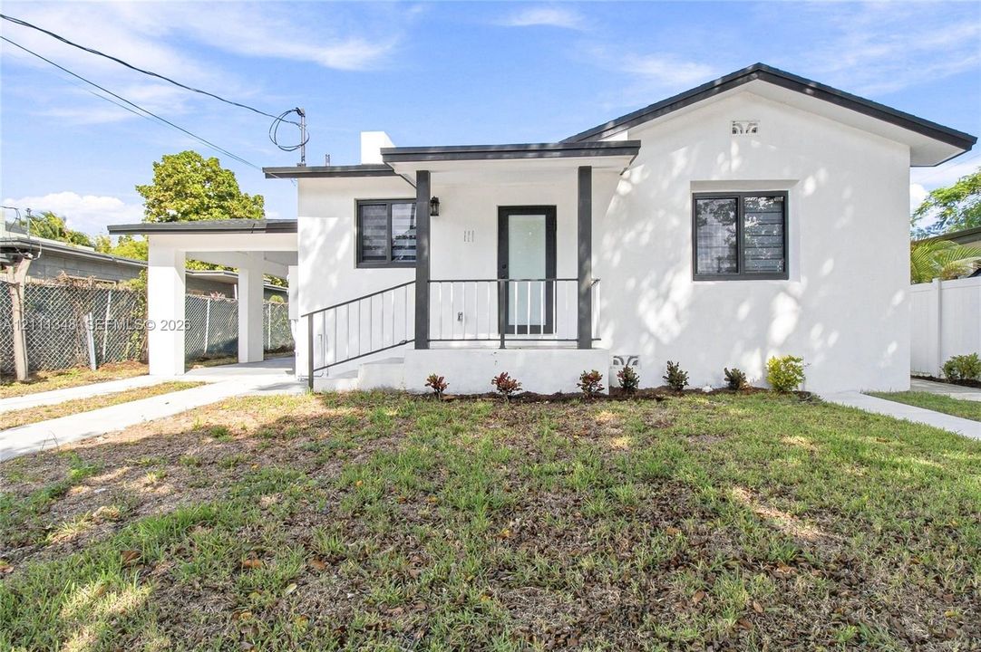 Single-story residence featuring a covered front porch, metal railing, attached carport, and dark-framed window accents