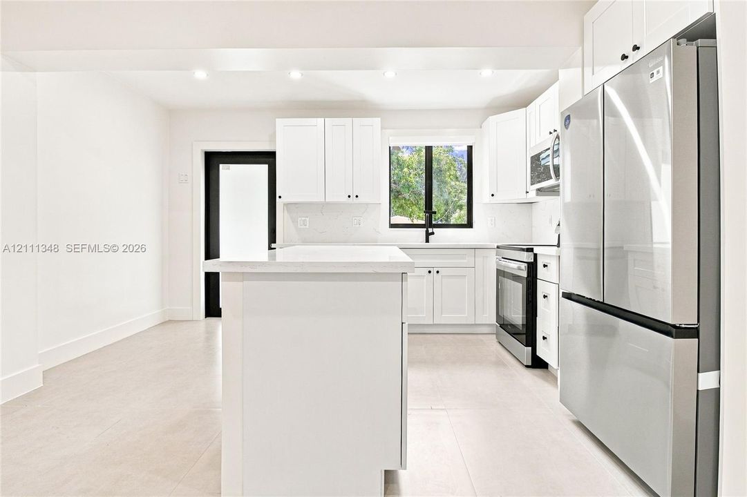 Kitchen featuring white cabinetry, center island with stone countertop, stainless steel appliances, recessed ceiling lighting, and matte black plumbing fixtures