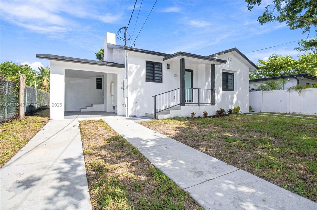 Stucco exterior residence featuring a covered carport, concrete driveway, and front entryway with metal railings