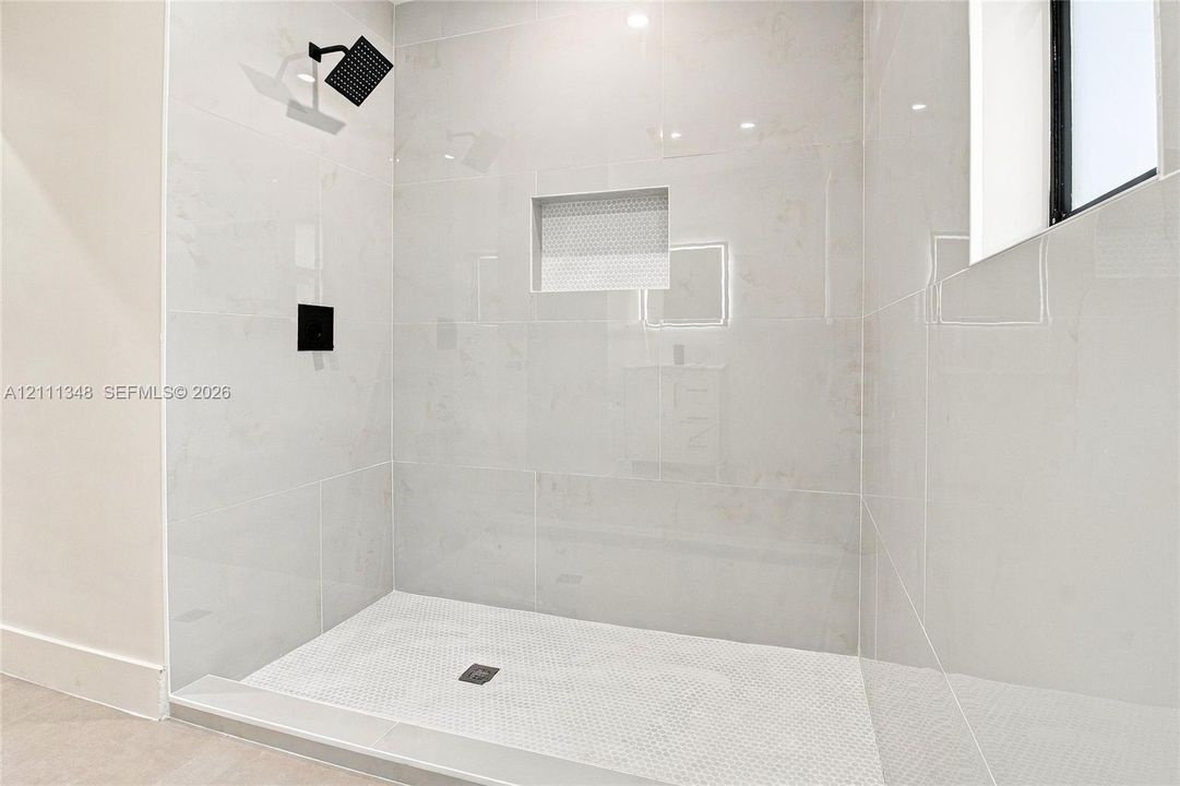Walk-in shower featuring large-format wall tile, a recessed tiled niche, a hexagonal mosaic tile floor, and matte black plumbing fixtures