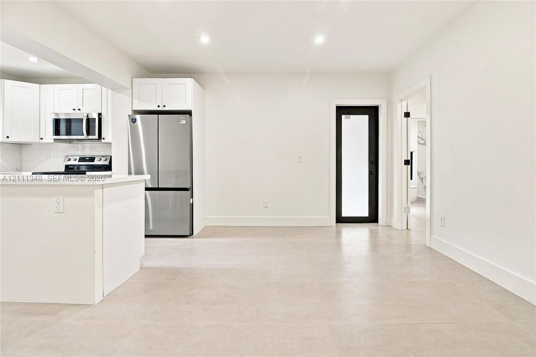 Kitchen featuring white cabinetry, stainless steel appliances, large-format neutral floor tiling, and a black-framed glass door