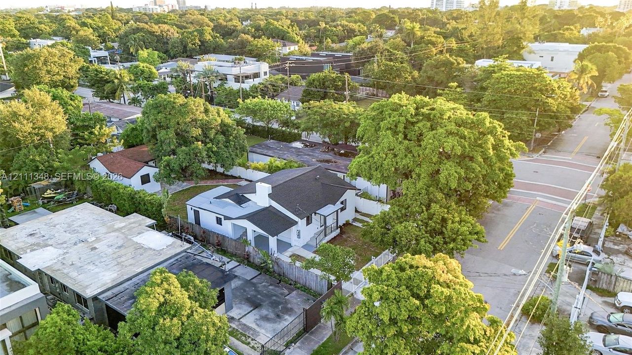 Aerial perspective of a single-story residence featuring a shingled roof, white exterior siding, concrete driveway, and a fenced perimeter