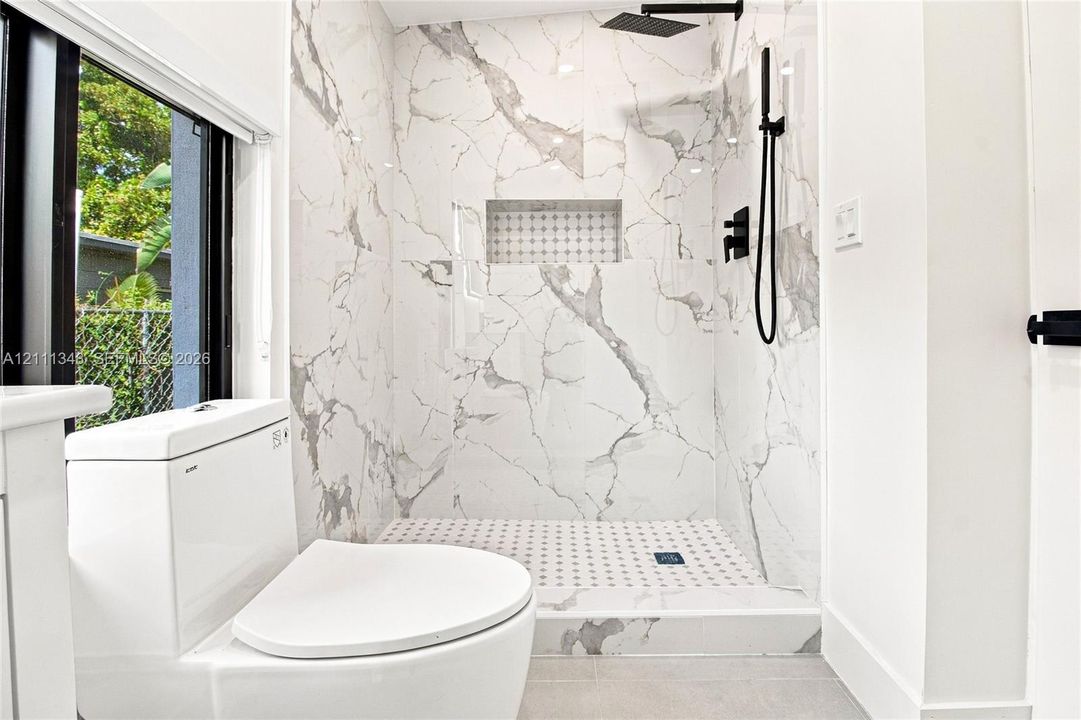 Walk-in shower featuring large-format stone-patterned tile walls, a built-in recessed niche, and matte black rain shower head with handheld attachment