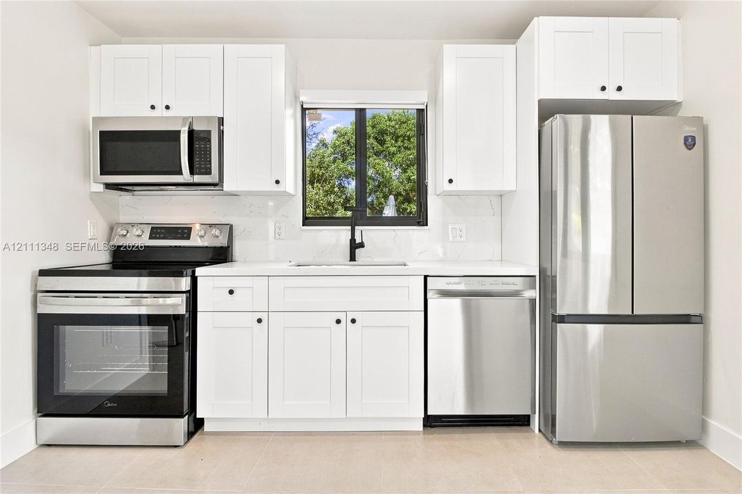 Kitchen featuring white Shaker-style cabinetry, stainless steel appliances, solid surface countertops, a matte black faucet, and a tile backsplash