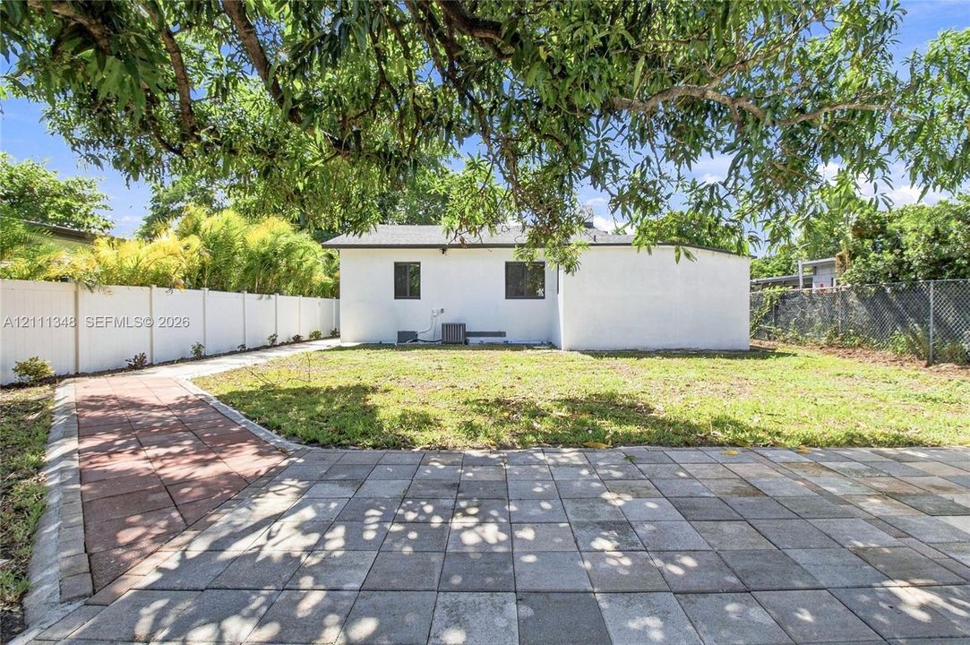 Backyard featuring a paved patio, a stone walkway, a vinyl privacy fence, and mature trees