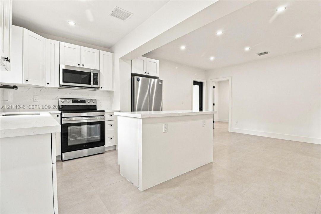 Kitchen featuring white shaker-style cabinetry, quartz countertops, stainless steel appliances, a central island, and recessed lighting