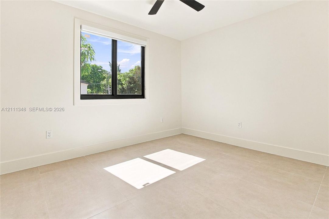 Neutral-toned tile flooring, minimalist white walls, and a black-framed window featuring multi-pane glass, complemented by an overhead ceiling fan