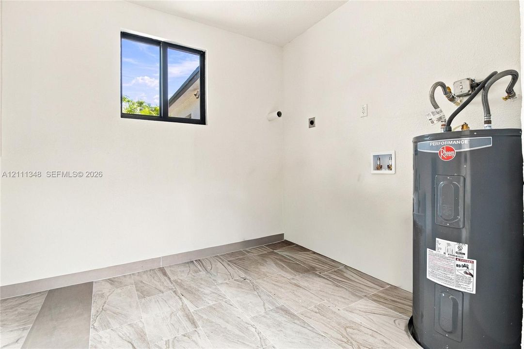 Utility area featuring large-format tile flooring, a horizontal sliding window with black trim, and an installed water heater