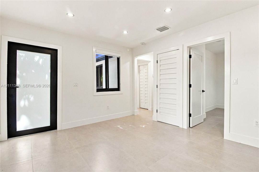 Neutral-toned tile flooring, recessed ceiling lighting, high-contrast black-framed exterior door with frosted glass panel, and white solid-core interior doors with matte black hardware