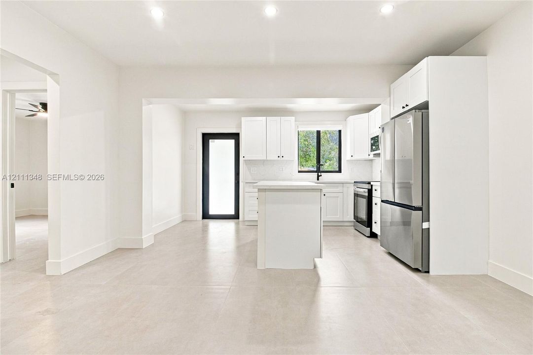 Kitchen featuring white shaker-style cabinetry, central island, stainless steel refrigerator, recessed lighting, and large-format tile flooring