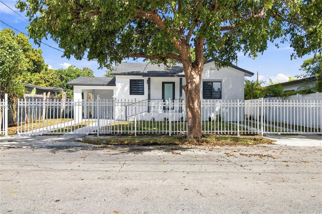 Single-story residence featuring a white exterior, covered carport, metal perimeter fencing, and louvered windows