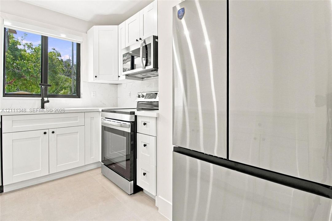 Kitchen featuring white shaker-style cabinetry, stainless steel appliances, a built-in microwave, stone-finish countertops, and a single-basin sink with a matte black faucet