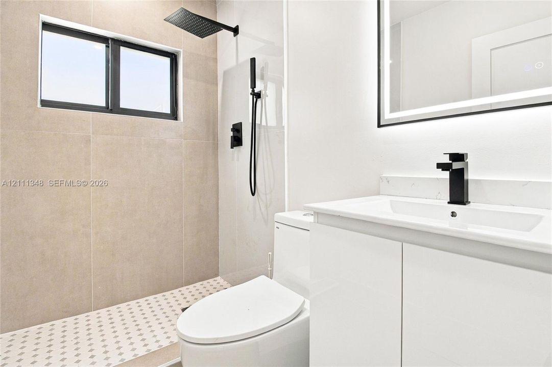 Bathroom featuring a walk-in shower with large-format tile surround, rainfall showerhead, and a separate handheld sprayer