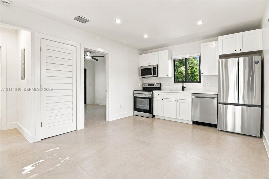 Kitchen featuring white cabinetry, stainless steel appliances, neutral tile flooring, recessed lighting, and a louvered door
