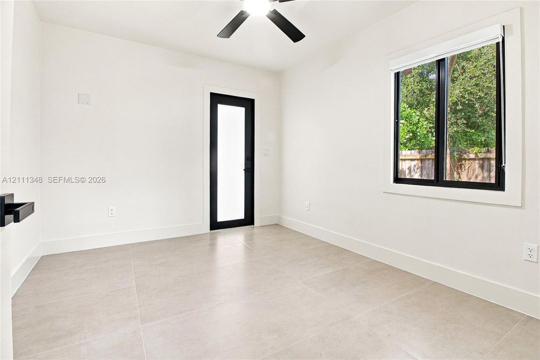 Neutral-toned tile flooring, black-framed door with a glass panel, window with black trim, and a ceiling-mounted fan with matte finish blades