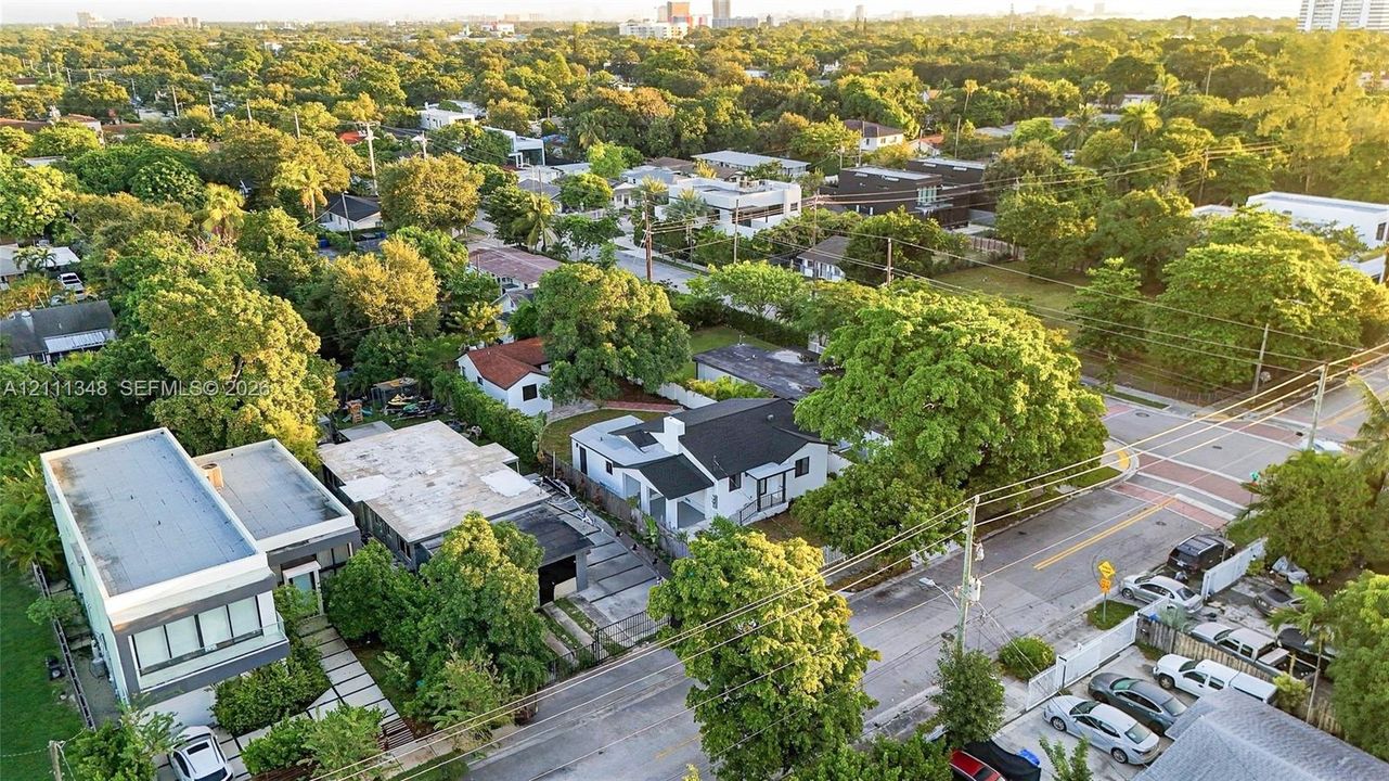 Aerial perspective of a corner lot property featuring mature shade trees, a paved concrete driveway, and a multi-level structure with a flat roof profile
