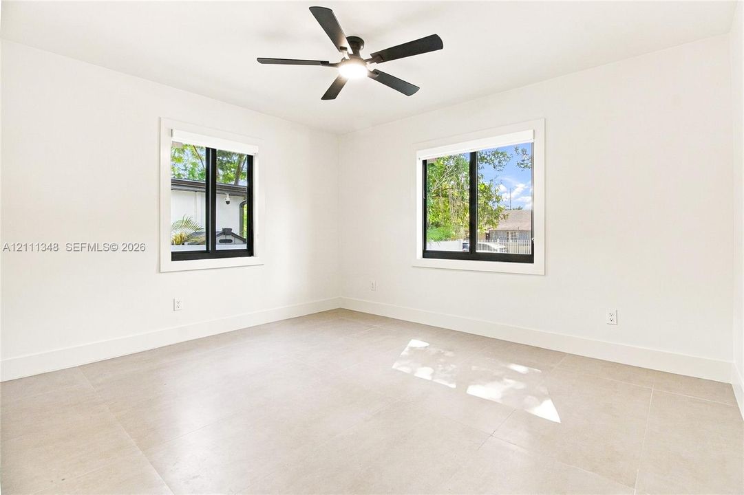 Neutral interior featuring large-format tile flooring, matte black window frames, and a modern ceiling fan