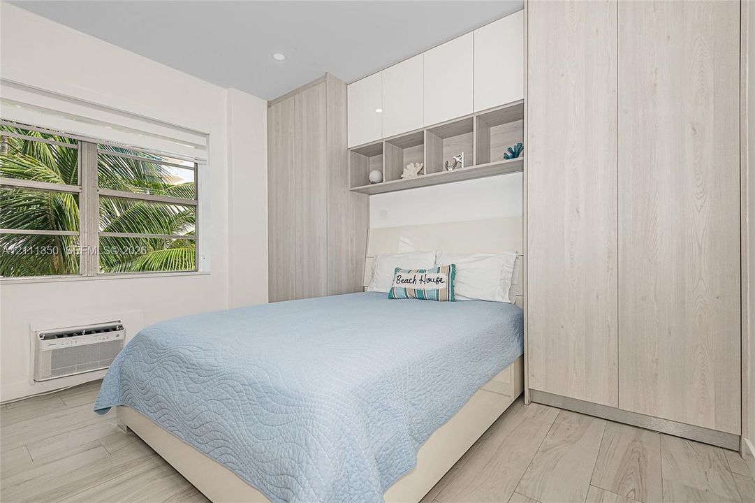 Custom built-in cabinetry featuring high-gloss upper cupboards, light wood-finish storage, and integrated display shelving, complemented by wood-finish flooring and a multi-pane horizontal window