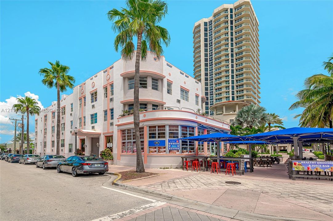 Art Deco exterior featuring a rounded façade, expansive multi-pane windows, and integrated outdoor seating area with overhead blue shade structures