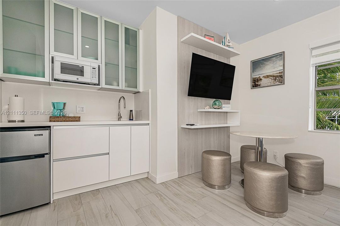 Kitchenette featuring white cabinetry with frosted glass inserts, integrated microwave, stainless steel sink, wood-finish flooring, and a decorative wall accent with built-in floating shelving