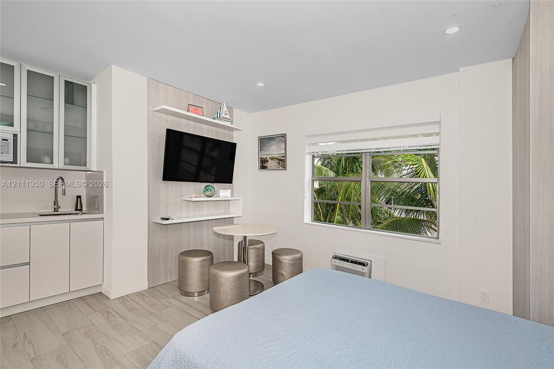 Kitchenette featuring white cabinetry with glass-front uppers, a stainless steel undermount sink, light wood-finish wall paneling, built-in shelving, and large-format tile flooring