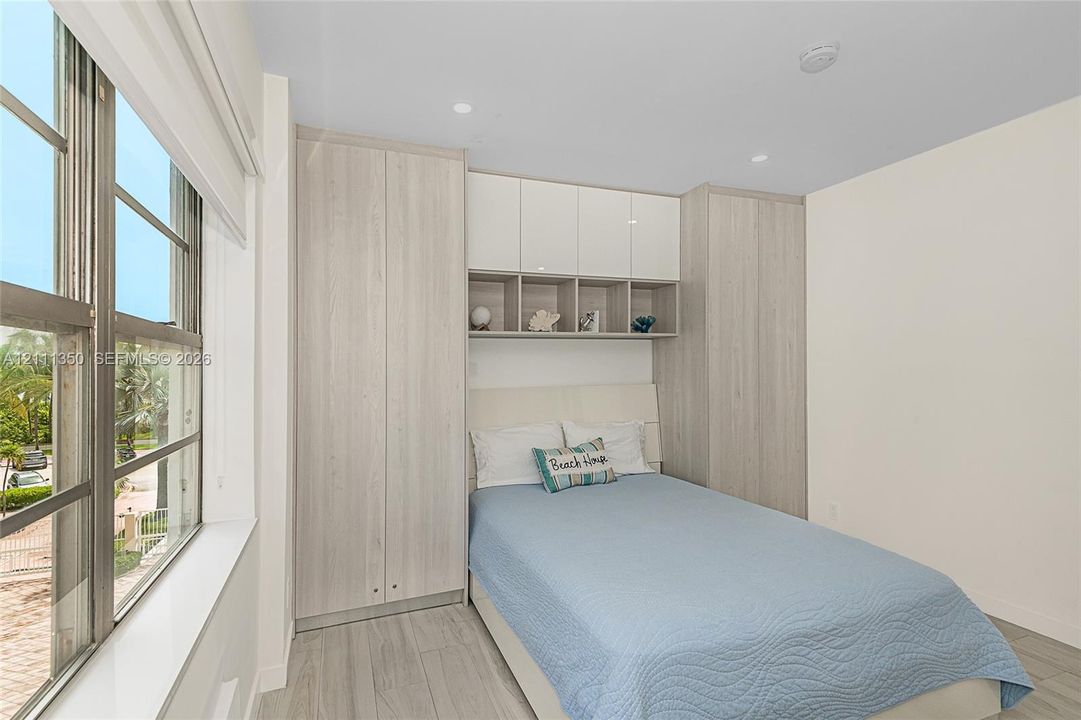 Built-in light-tone wood-finish cabinetry, gloss-finish upper storage, open shelving, large windows with horizontal blinds, and wood-finish flooring