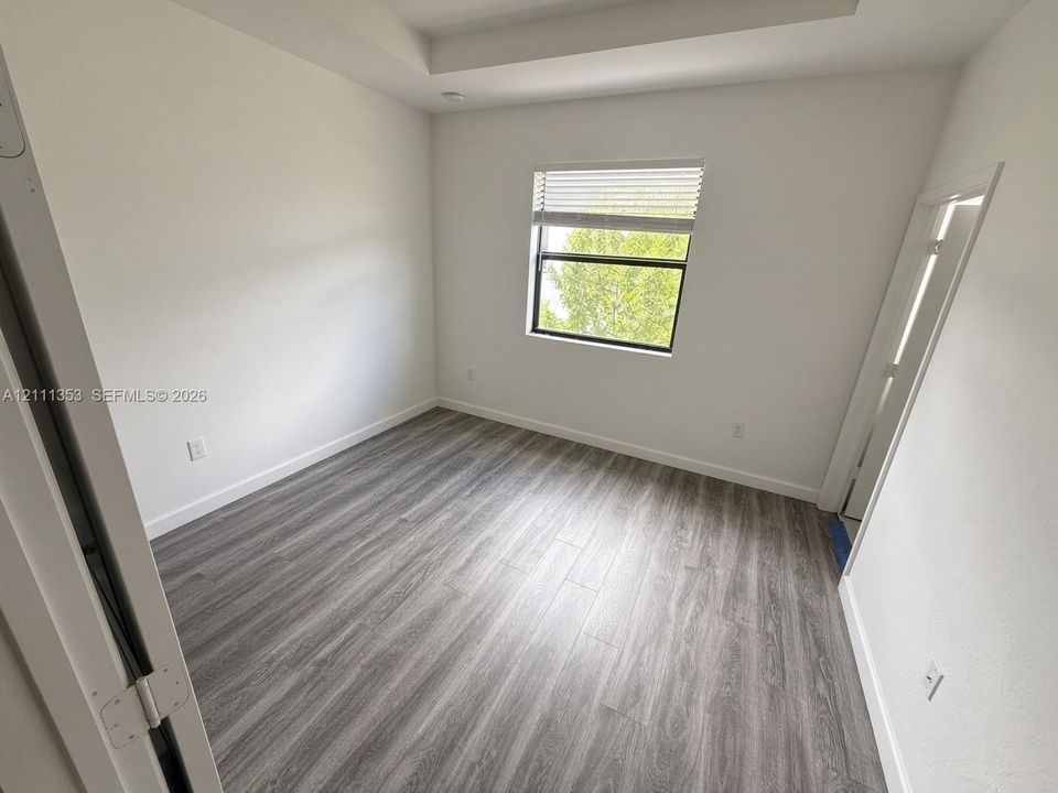Neutral-toned wood-finish flooring, tray ceiling, and a single-pane window with horizontal blinds