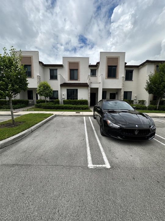 Modern multi-story exterior featuring light-toned stucco, stone veneer accents, horizontal slat detailing, and concrete sidewalks