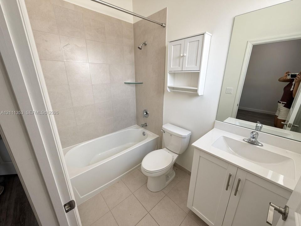Bathroom featuring a white vanity cabinet with a stone-top surface, wall-mounted storage cabinetry, large vanity mirror, and a tiled tub surround
