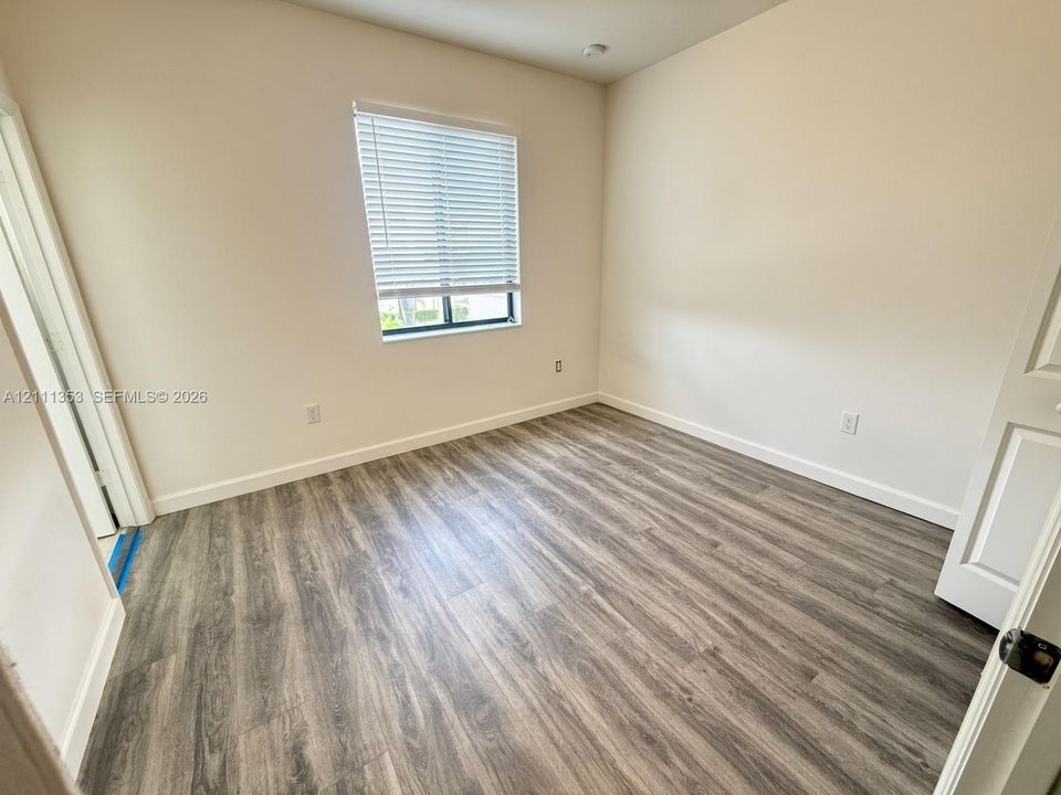 Neutral-toned interior space featuring wood-finish flooring, a single window with horizontal blinds, and a paneled interior door