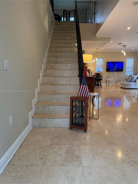 Staircase featuring stone-finish treads, decorative metal railings, and polished stone tile flooring
