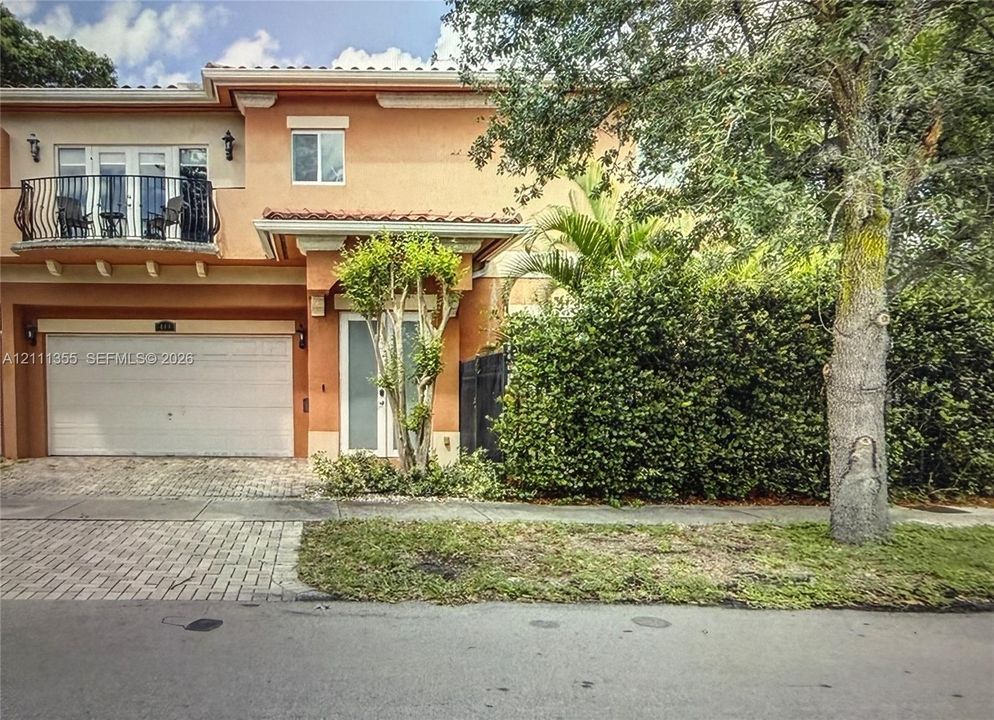 Stucco exterior featuring an arched second-story balcony with metal railing, a paved driveway, and covered entryway
