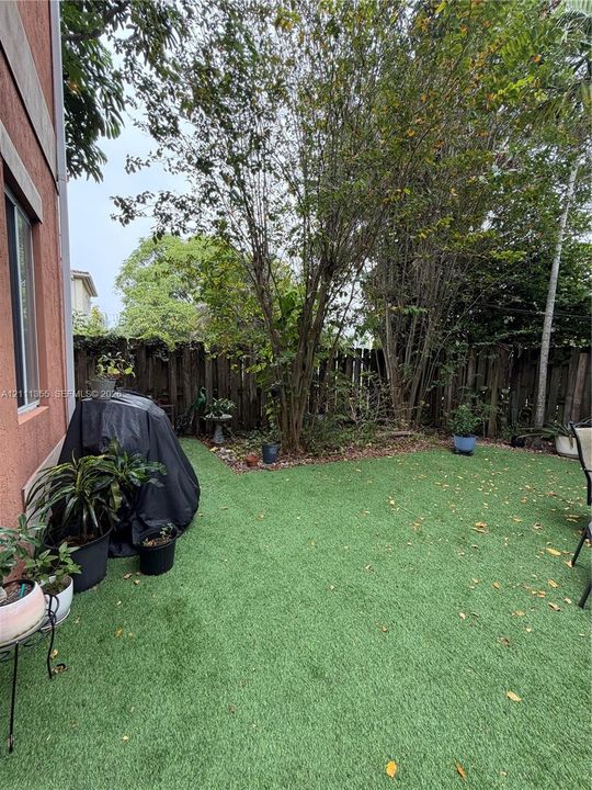 Enclosed backyard featuring synthetic turf, mature trees, and a wooden privacy fence