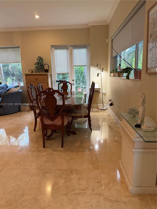 Polished stone flooring, crown molding, and glass-paned double doors with integrated shades